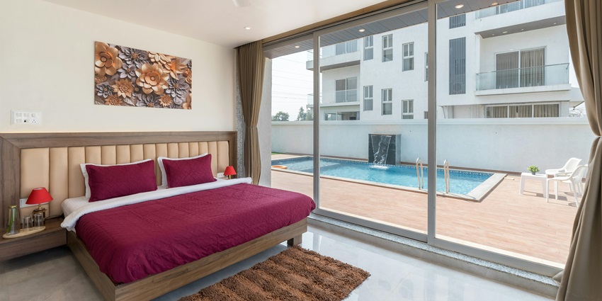 Interior of a hotel room with a bed, lamps on the tables and a pool outside of the room