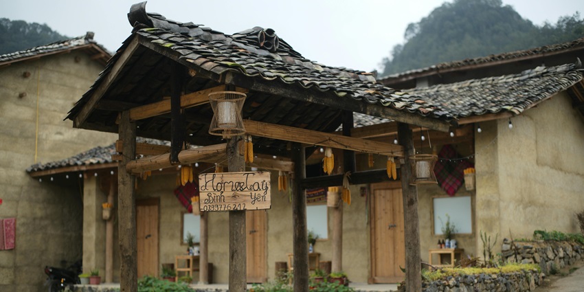 Old aesthetic homestay entrance with a hanging sign board, lamps and hills in the back.