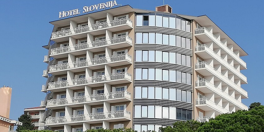 A multi-story hotel building with a sign "HOTEL SLOVENIJA" against a clear blue sky