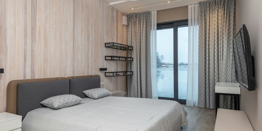 A modern bedroom with a gray upholstered headboard, a neatly made bed, light wood paneling
