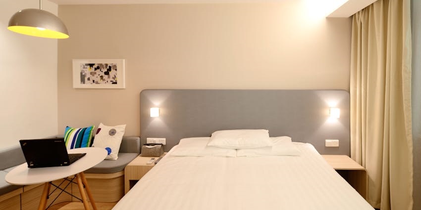 A clean, modern hotel room with a neatly made bed, a laptop on a small table, a gray couch