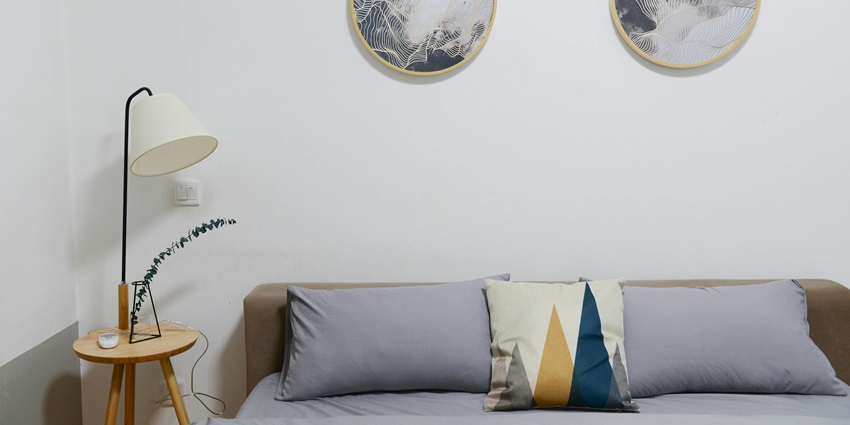 An image showing a hotel bedroom featuring a brown wooden bed with a grey comforter set.