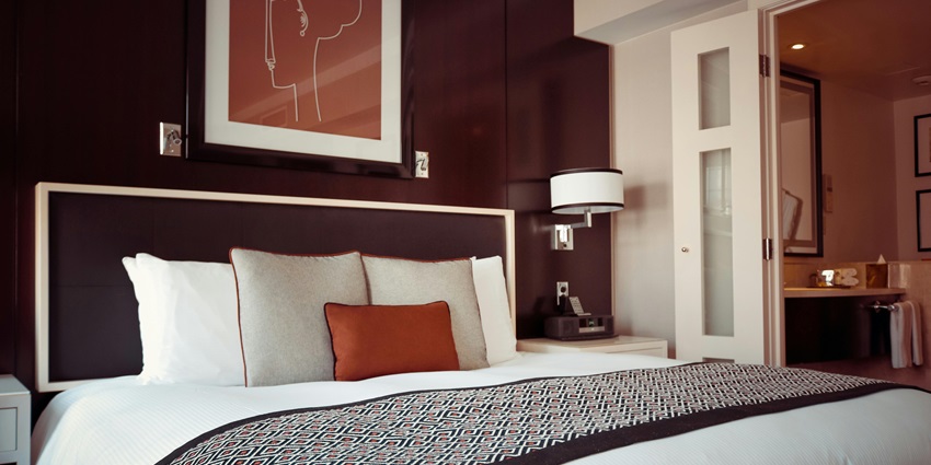 An image showing a cosy hotel room with a bed in black and grey bedspread and pillow.