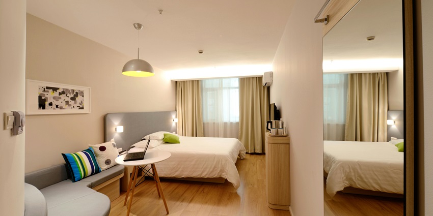 An image showing a hotel's stylish bedroom interior setup with warm lighting and decor.
