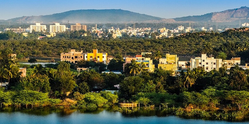 A lot of greenery, colourful houses, and buildings around a water body with mountains