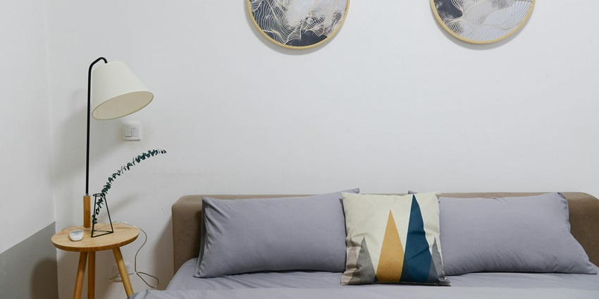 An image showing a well-designed hotel room with a nightstand, desk lamp, and a stylish bed.