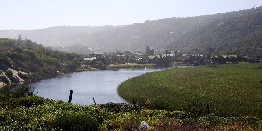 One of the lakes of the Wilderness Lake System in Western Cape Town, showing homes on its coast and mountains nearby