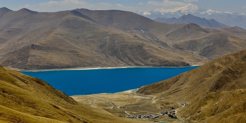 Yamdrok Lake with a blue water body surrounded by sandy shorelines and sandy mountains.