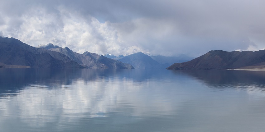 Lake with a large still water body surrounded by rocky mountains partially covered in clouds