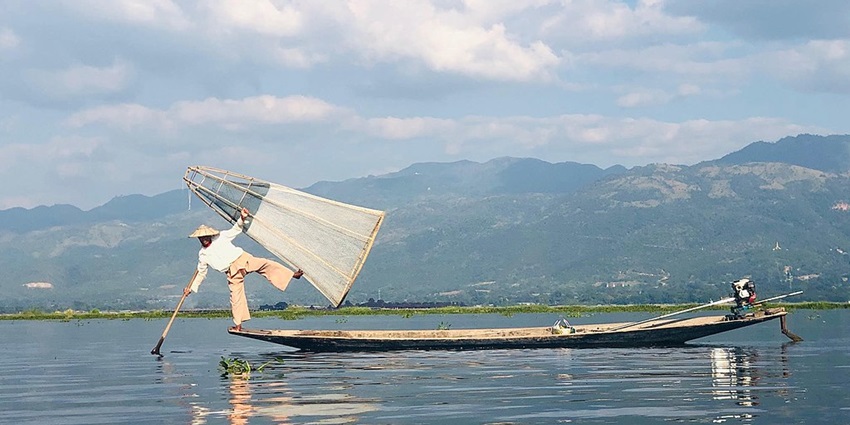 A panoramic view of the lake with clear water, traditional boats and lush green mountains.