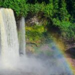 The Agbokim Waterfalls Nigeria is seen surrounded by dense greenery and a rainbow mist.