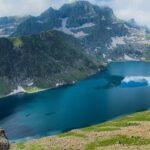 Lake in Kashmir with a deep blue water body, a person sitting on a rock and greenery