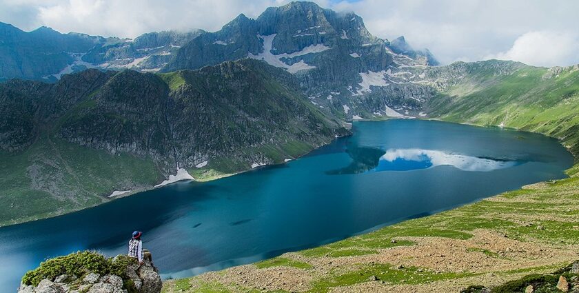 Lake in Kashmir with a deep blue water body, a person sitting on a rock and greenery