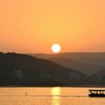 An image of Lake Pichola in Udaipur at sunset, with silhouettes of boats and hills visible