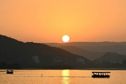 An image of Lake Pichola in Udaipur at sunset, with silhouettes of boats and hills visible