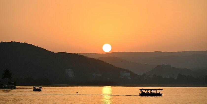 An image of Lake Pichola in Udaipur at sunset, with silhouettes of boats and hills visible