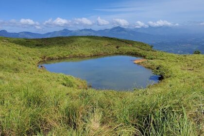 Chembra Lake, a unique heart shaped lake in India with distant mountains under clouds.