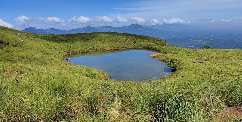 Chembra Lake, a unique heart shaped lake in India with distant mountains under clouds.