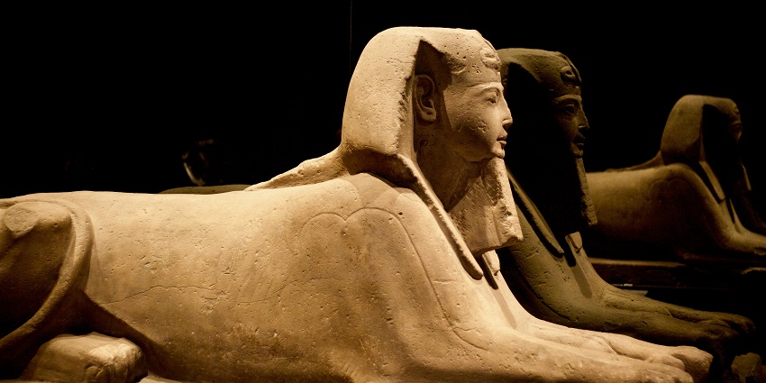 Ancient Egyptian statue displayed in a dimly lit museum exhibit, emphasizing their details.
