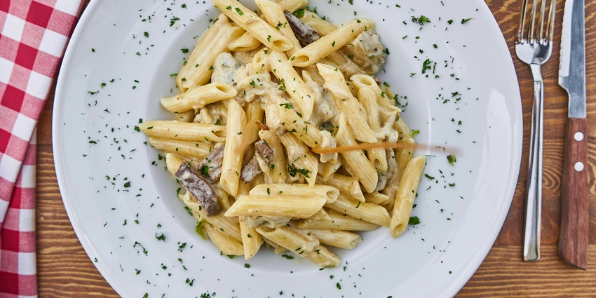 White sauce pasta has been served on a white plate garnished with parsley sprinkles
