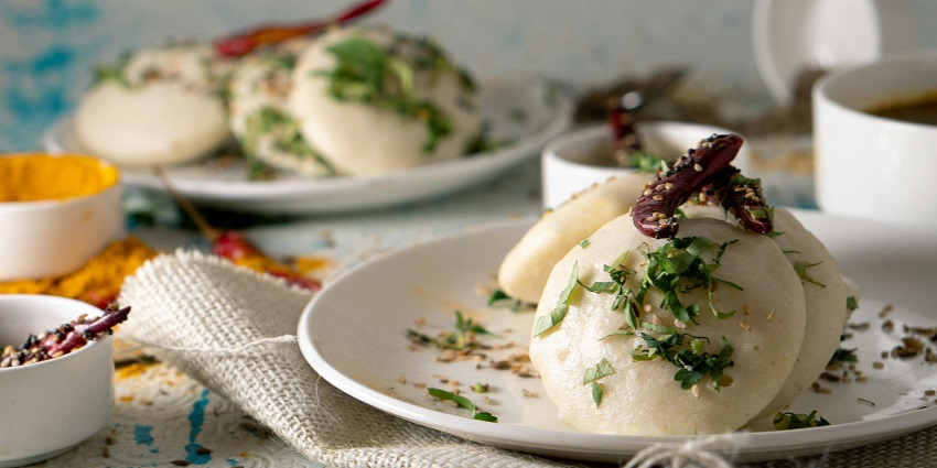 Image of delectable Idli served on a plate with chutney on the side and veggies