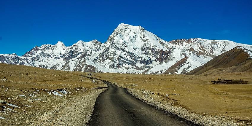 Highway in Sikkim with a narrow road, sandy plains and snow-covered mountains ahead