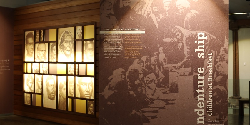 An image of the Aapravasi Ghat with an exhibit detailing indentured labourers' voyage to Mauritius, featuring photos and portraits.