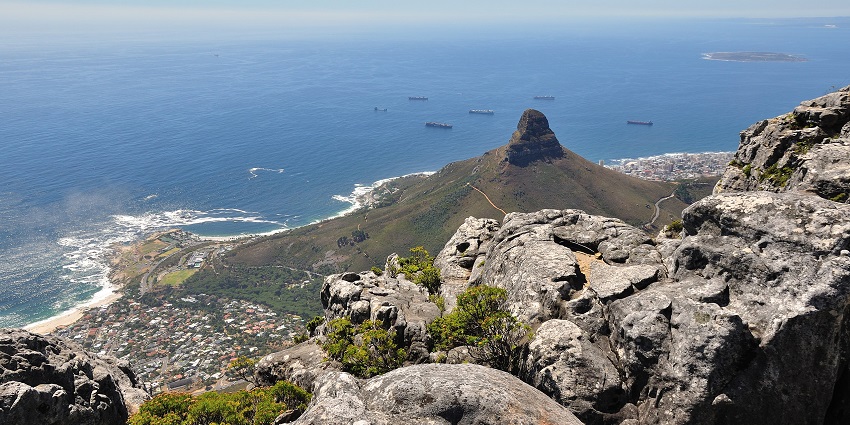 An image of Cape Town’s Lion’s Head peak overlooking the Camps Bay Beach, with vegetation, vast ocean, and clear skies.