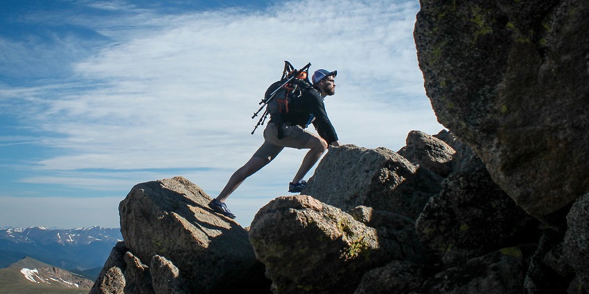 A man climbing a steep gray rock face during daytime