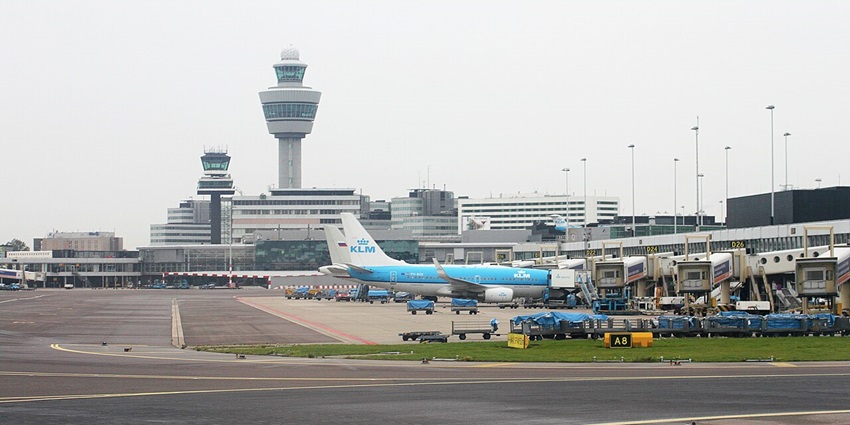 A bustling scene at Amsterdam Airport Schiphol with planes, vehicles, and a terminal.