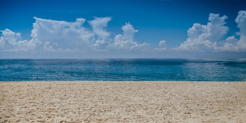 An image of a beach with sandy shores, blue ocean waves, and a cloudy sky, similar to the experience at Rose Hill, Mauritius.