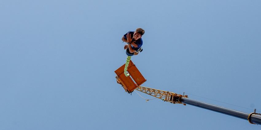 A man mid-air during bunjee jumping in South Goa, free-falling with arms spread wide against a scenic outdoor backdrop.