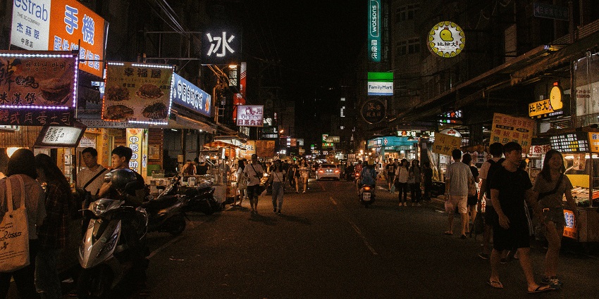 A night-time scene of this market, with bright lights and busy shoppers exploring different stalls.
