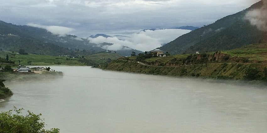 Large waterbody of Bhutan with green shores and buildings on the hills covered in mist