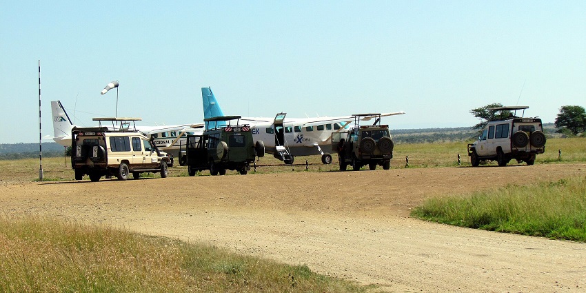 Air strip with a blue and white aeroplane parked surrounded by vehicles and a dirt runway