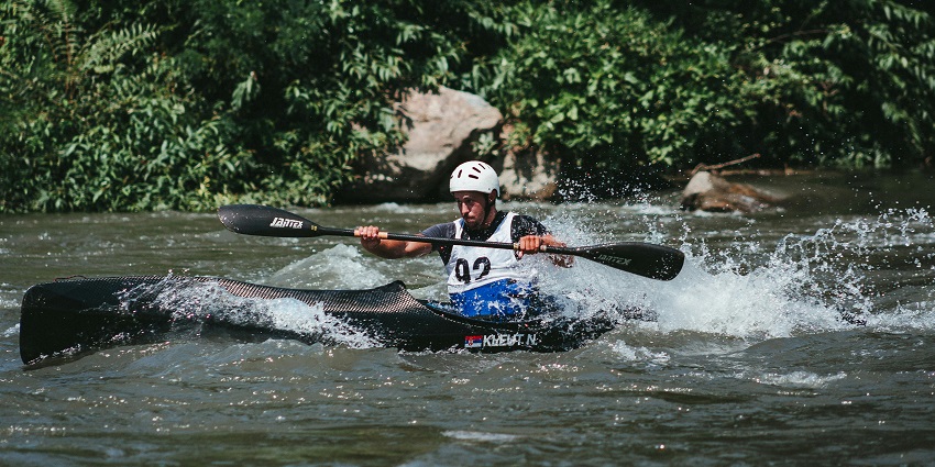 Professional kayaker in a black kayak and holding a paddle with helmet and safety jacket on