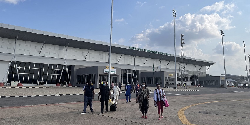Akanu Ibiam International Airport with a blue sky as passengers with luggage exit the terminal