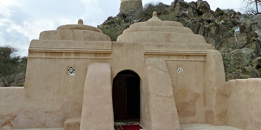A scenic view of Al Badiyah Mosque, the oldest mosque in the UAE, surrounded by rugged hills.