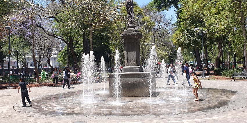 Monument of Beethoven in the middle of Alameda Central, with people passing by and big trees