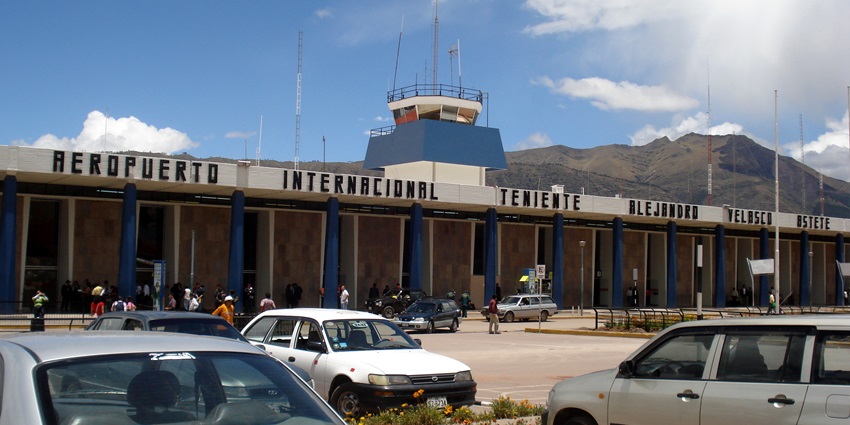 Alejandro Velasco Astete International Airport with parked cars, terminal with airport name visible under clear blue sky