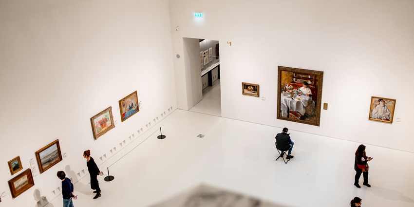 People viewing and photographing the art hanging on the white walls of a museum