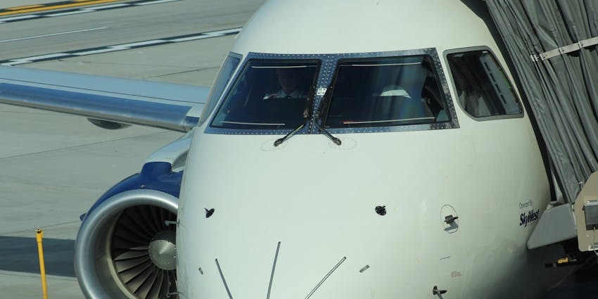 Airplane landing at an airport runway, vehicles parked on the side and distant buildings.