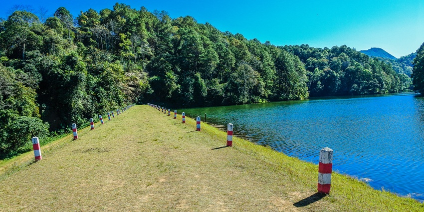 View of the blue waters’ lake, dense trees, grass, sky and some temporary shelters.