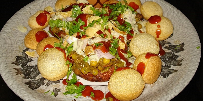 An image of Aloo Tikki garnished with cilantro, served with tamarind chutney, yogurt, and spices, on a plate