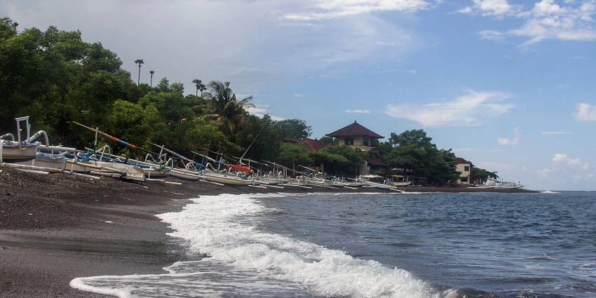 Scenic view of Amed Beach, with its calm waters, black sand, and diving boats.