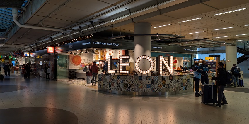 A few passengers standing in a queue at a fast food shop at Amsterdam Airport in Europe.