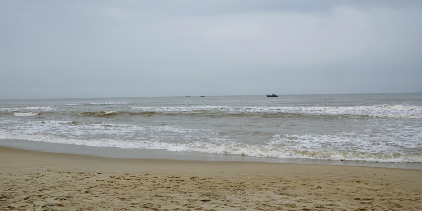 A beach scene with gentle waves rolling onto the sandy shore under an overcast sky