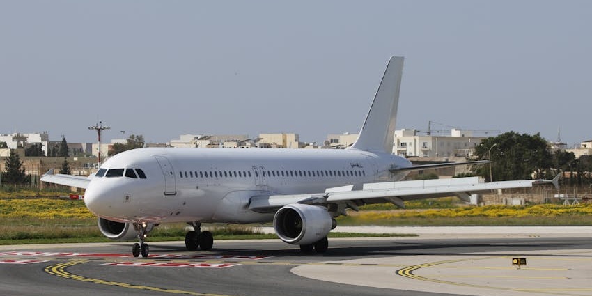 A white and blue airplane on a runway with lush greenery all around at the Anatom Airport