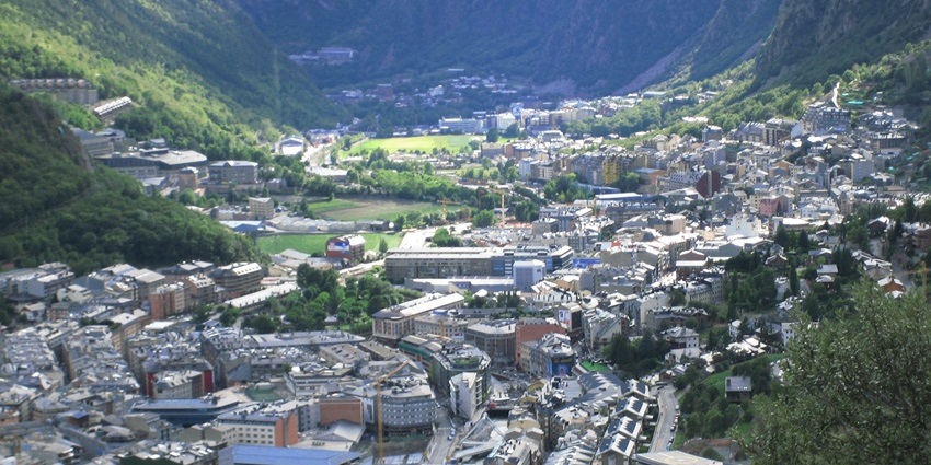 Aerial view of a city in a green valley, surrounded by mountains with winding roads.