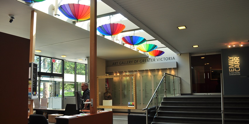 An image of the Art Gallery of Greater Victoria's interior showing the reception desk, umbrellas, and exhibition signage.